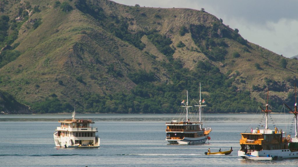 Several boats float on the calm ocean near hills.